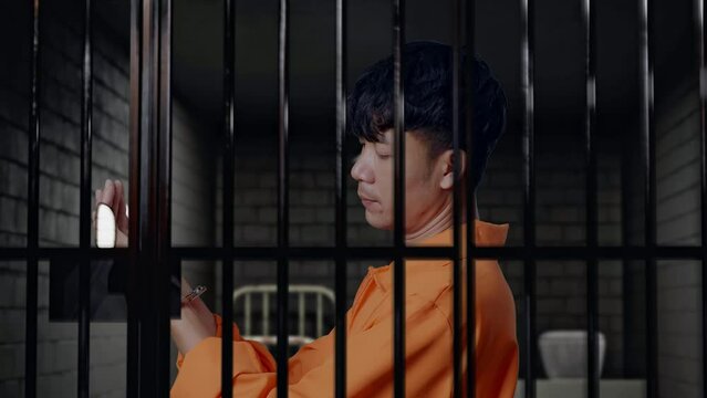 Close Up Side View Of Asian Male Prisoner Standing In Prison, Looking At Handcuffs And Shaking His Head Being Upset On What He Did