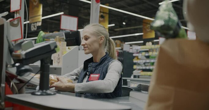 Female cashier scanning food products and giving to customer packing in paper bag at cash register in supermarket. Shopping and retail store concept.