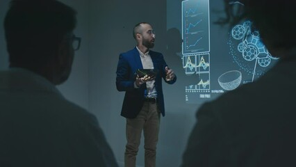 Full over-shoulder shot Middle Eastern male pharmaceutical sales representative with tablet computer presenting new medication or therapy to doctors at conference, speaking about its benefits