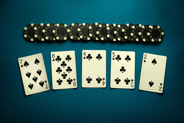 Chaotically lying playing cards and black chips on a blue table in a poker club. The concept of an...