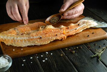 Cooking fish steak by the hands of a chef on the kitchen table. Low key concept of fish diet.