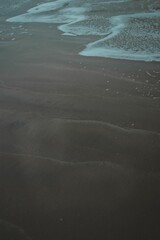 Vertical shot of a sandy beach with the sea waves washing the shore