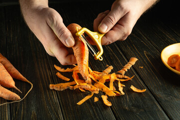 Chefs hands peel carrots with a vegetable peeler to prepare a vegetable drink or smoothie. Low key concept for making a vegetarian breakfast drink.