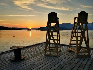 Rustic wooden lifeguard chairs at the edge of a pier overlooking a tranquil lake in Norway