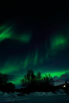 Vertical shot of a hill covered in snow during the Northern Lights
