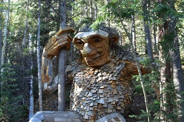 Isak Heartstone wooden sculpture on a grassy terrain, with a backdrop of trees and logs