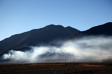 Idyllic landscape with a mountain in the background and smoke billowing from a field