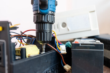 Close up Hand of man using a drill to remove the screws from the UPS battery backup for personal...