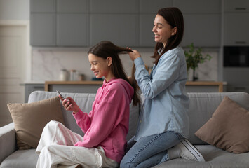 Mother spending time with teen daughter at home, braiding long hair of girl child before school in morning. Mother-daughter date concept