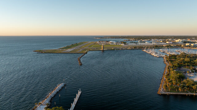 Sunrise over Albert Whitted Airport in St. Petersburg, with calm waters and docked boats nearby, cityscape in the distance.