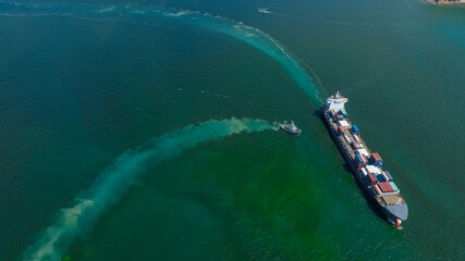 Aerial top view of cargo ship with contrail in the ocean sea ship carrying container and running from container international port smart freight shipping by ship service.