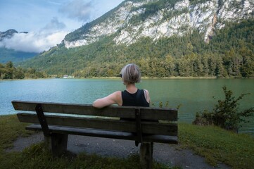 Rear view of a female seated on a bench in a park near a lake in the Tyrolean Alps
