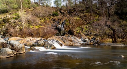 Landscape of a stream with long exposure surrounded by rocks and greenery