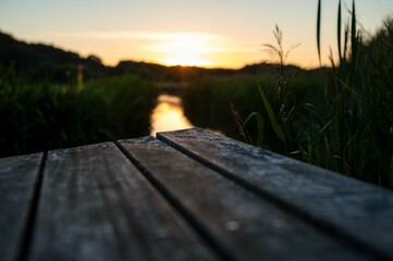Sunset scenery viewed from the end of a wooden boardwalk, with a tranquil river in the background