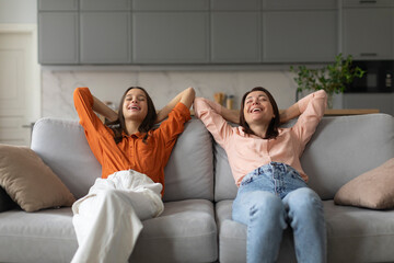 Calm mom and daughter relax on couch hands over head, lying on sofa resting with eyes closed,...