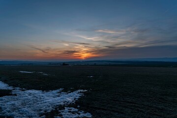 Fototapeta premium the sun is setting over a snow covered field with patches of grass