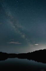 the stars shine in the sky above the calm water and a forest