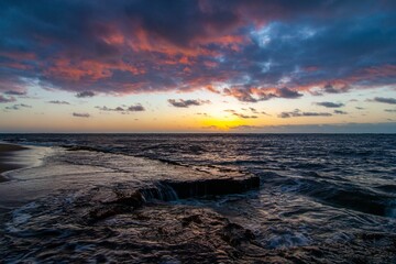 Fototapeta premium Scenic beach landscape with turbulent waves crashing against the shore against the cloudy sunset sky