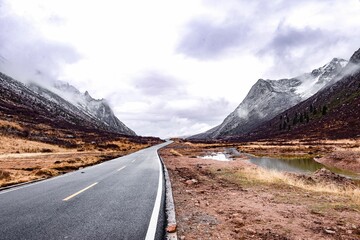Wintery road with snow-dusted mountains in the distance on a cloudy day