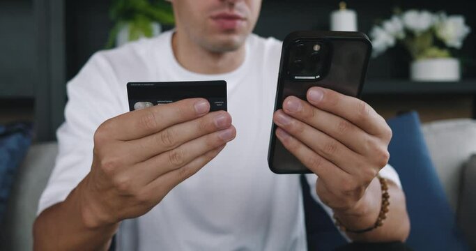 Man seated, inputs bank card into smartphone, enabling online payments. Ease of online payments clear, navigating daily digital transactions. Online payments merge security, convenience.