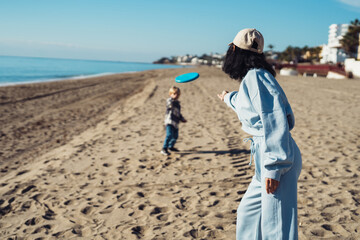 Mom plays frisbee with a boy in the sea. young woman and boy playing frisbee on the seashore. outdoor game with a child at sea