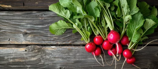 Poster A bunch of radishes with vibrant green leaves resting on a wooden table, ready for culinary use. © FryArt Studio