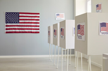 Side view of white empty voting booths at polling station with American flag. Interior of vote center ready for presidential elections in the United States. Democracy and election day concept.