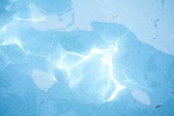 Surface of blue swimming pool, reflection on blue water, swirl pattern texture, tiles. Leaves in dirty water, opened swimming pool. Background, backdrop with copy space.