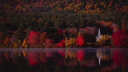 Picturesque church stands by the tranquil waters of a lake, with lush trees in red framing the scene