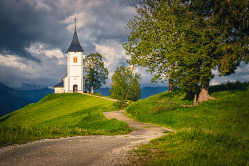 Winding rural road and Saint Primoz mountain church, Jamnik, Slovenia - 772315550