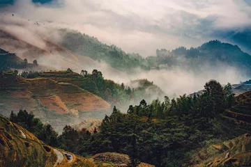 Fotobehang Landscape of rolling hills, shrouded in mist, with a backdrop of mountains and a scattering of trees © Wirestock