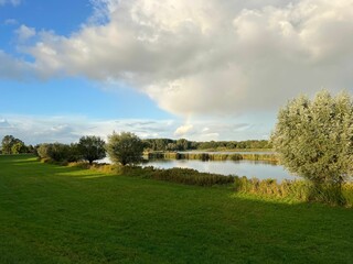 Scenic view of Zwarte Water river near a green field on a cloudy sunny evening
