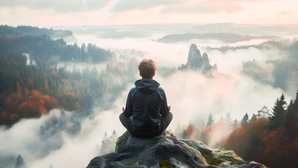 Deurstickers Person sitting on a rock meditating in a foggy, forested landscape during a tranquil sunrise. © apratim