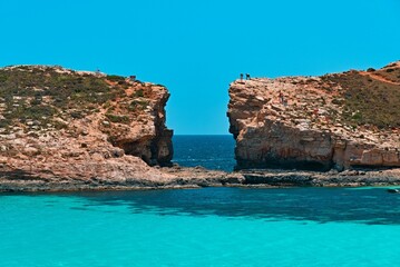 Tranquil scene of two small stones resting on the beach of a crystal clear lake with people on top