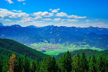 Fototapeta premium Scenic view of Bavarian Alps with green trees surrounding the peak and a clear blue sky overhead