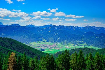Scenic view of Bavarian Alps with green trees surrounding the peak and a clear blue sky overhead