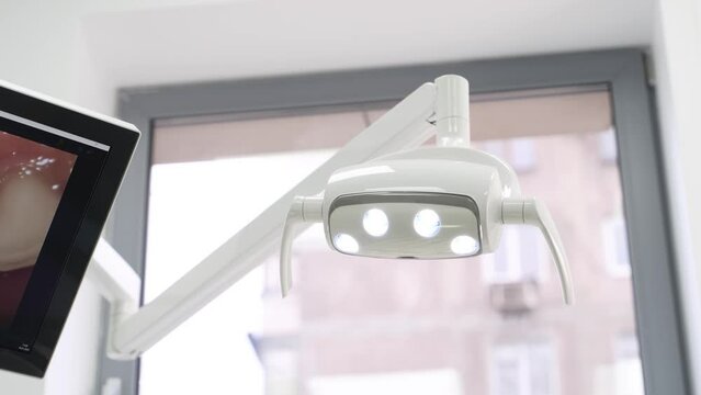 Dentist's hand turn on dental lamp by motion in modern dental office. Dental lamp with proximity sensor. Professional modern dental equipment in medical clinic. Concept of dentistry and teeth care.