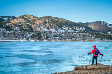 male hiker with trekking poles at a shore of frozen Horsetooth Reservoir near Fort Collins,...