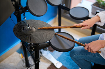 Close-up hands of teen boy musician creating rhythm of music while banging drums in stylish retro...