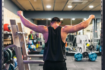 Anonymous Athlete Stretching Arms in Gym, Back View. Back view of anonymous athlete stretching arms in gym, cap and tank top on.