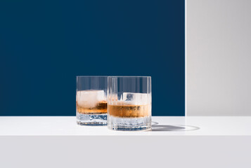 Dos vasos de whisky con hielo sobre un fondo azul	

