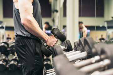 Anonymous Athlete Picking Up Dumbbells in Gym, Side View. Anonymous muscular athlete in gym, picking up two dumbbells, side view.