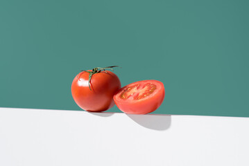 Un tomate maduro entero y cortado por la mitad sobre un soporte blanco y fondo verde - obrazy, fototapety, plakaty