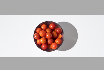 Tomates cherry maduros en un bol sobre fondo gris y blanco. Vista superior	