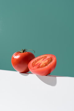 Un tomate maduro entero y cortado por la mitad sobre un soporte blanco y fondo verde