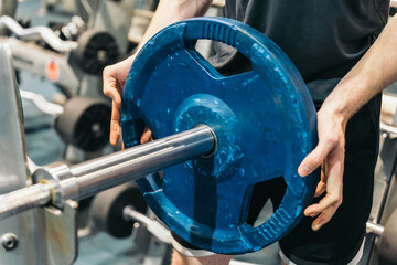 Anonymous Athlete Adjusting Weight Plate on Barbell in Gym. Anonymous athlete in gym, adjusting blue weight plate on barbell.