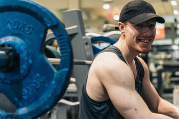 Side View of Relaxed Red-haired Athlete on Bench Press, Looking at Camera. Relaxed red-haired athlete in gym, resting on bench press, looking and smiling at camera.