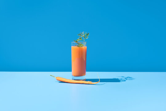 Jugo de zanahoria adornado con hojas verdes en un vaso transparente sobre fondo azul	