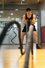 Muscular redhead man in tank top vigorously moving ropes in workout.