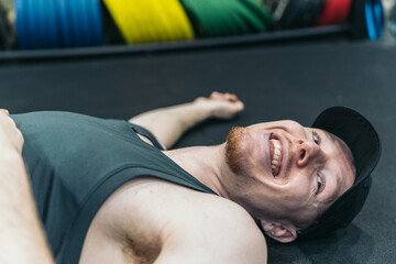 A smiling tired redhead athlete lies on the gym floor.